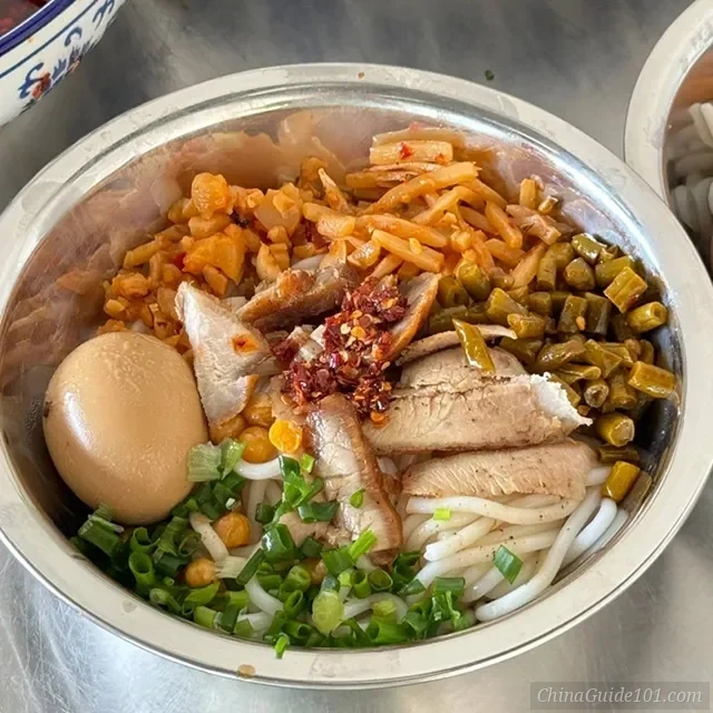 A bowl of authentic Guilin Rice Noodles (Mifen) with crispy pork belly, braised beef, peanuts, and sour beans, served dry-tossed.