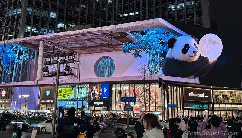 The massive naked-eye 3D LED screen in Chengdu Taikoo Li district at night, showing a giant panda holding a moon in a futuristic bamboo forest setting.