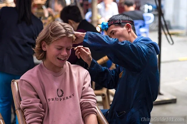 A professional ear cleaning master using specialized tools to provide a traditional Sichuan ear massage to a foreign tourist at People's Park in Chengdu.