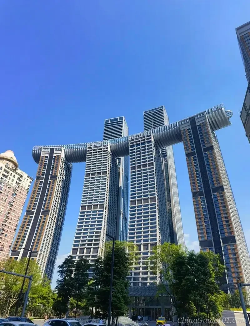 A low-angle view of the futuristic Raffles City Chongqing complex featuring four massive skyscrapers connected by 'The Crystal'—the world's highest horizontal skyscraper skybridge—against a clear blue sky.