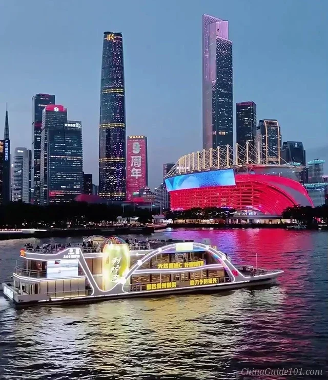 A Pearl River night cruise boat sailing past the illuminated Zhujiang New Town skyline. The Guangzhou IFC (West Tower) and CTF Finance Centre (East Tower) glow in the background alongside the red-lit Haixinsha Asian Games stadium