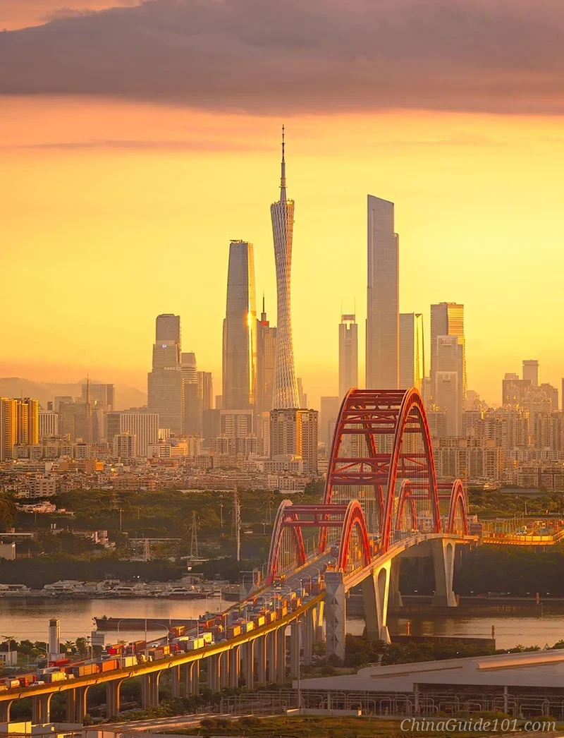 A panoramic sunrise over the Guangzhou skyline in 2026. The red arches of Xinguang Bridge span the waterway in the foreground, with the distant Canton Tower and CBD skyscrapers silhouetted against the golden morning sky.