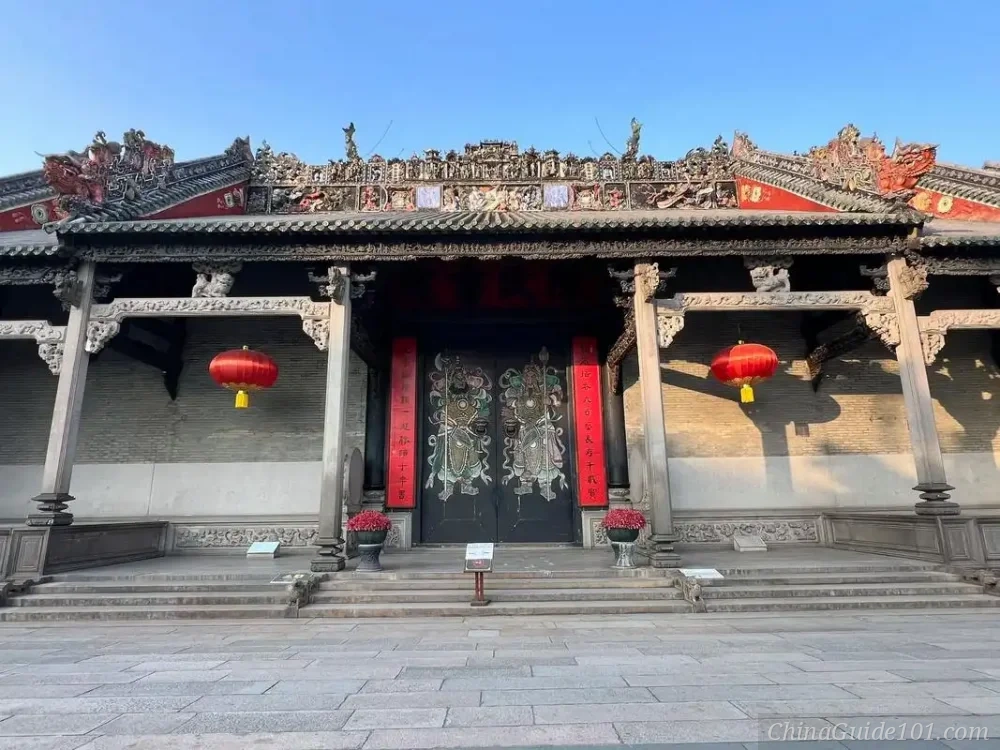 The grand main entrance of Chen Clan Ancestral Hall in Guangzhou. The image showcases the intricate 'Lingnan' style roof decorations, ceramic carvings, and the imposing black gate painted with traditional Chinese Door Gods (Menshen).