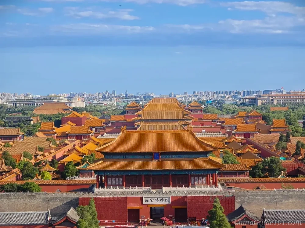 High-angle viewpoint of the Forbidden City in Beijing, showing the layered yellow roofs of the ancient palace complex stretching from the Gate of Divine Might toward the city skyline