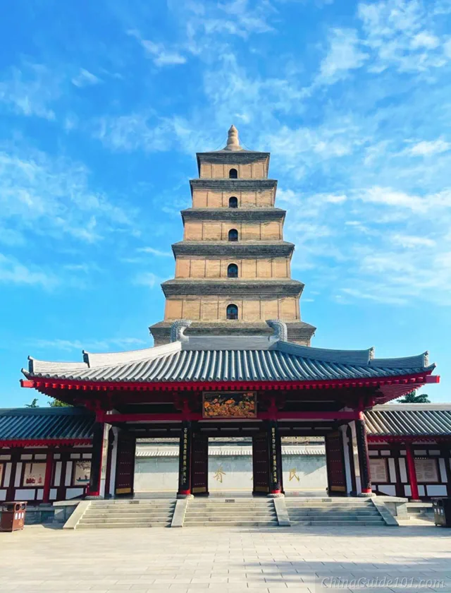 Front view of the seven-story Giant Wild Goose Pagoda in Xi'an, standing behind a traditional Chinese temple gate with a red and grey roof under a bright blue sky.