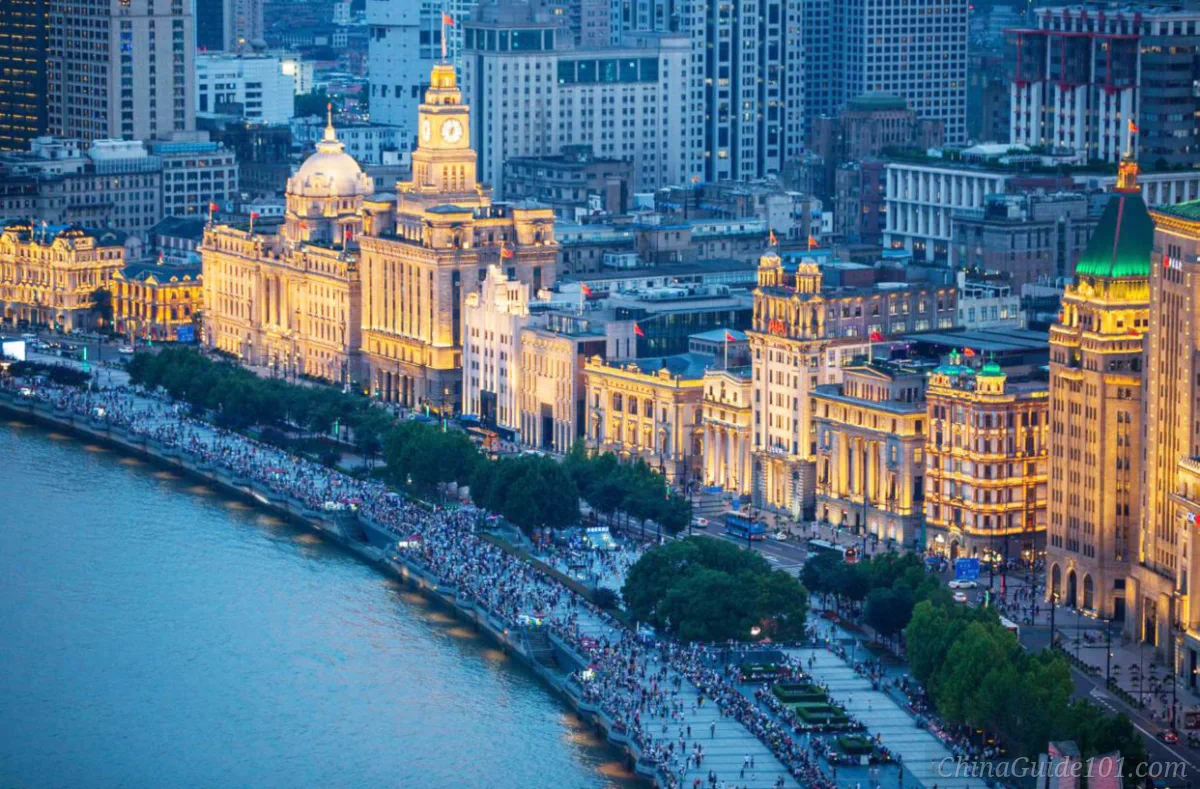 High angle view of illuminated historic European-style buildings and crowds on The Bund promenade in Shanghai at dusk