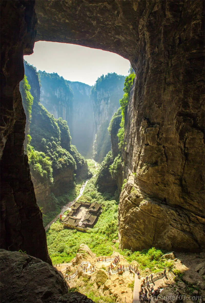 View through a massive natural limestone arch over Tianfu Posthouse and valley hiking trails at Three Natural Bridges, Wulong Karst UNESCO site near Chongqing