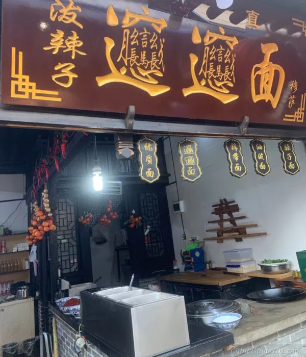 storefront of biangbiang noodle shop in xi'an, featuring huge chinese biang character on wooden signboard, traditional shaanxi noodle restaurant