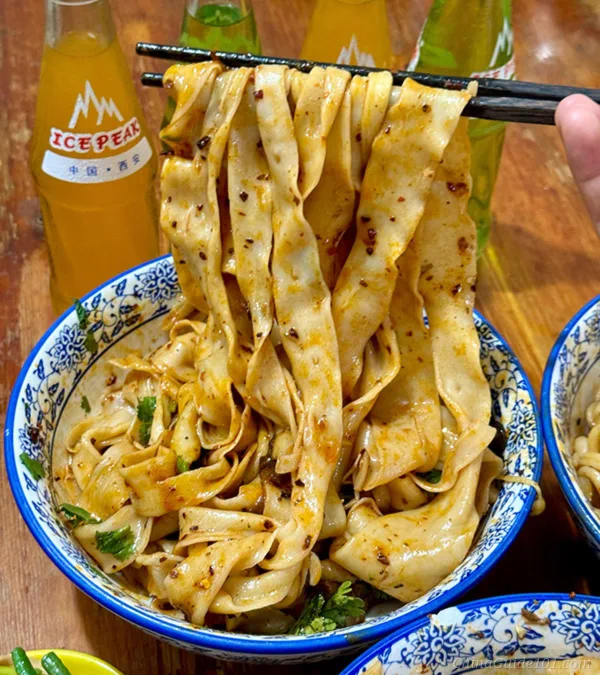 xi'an biangbiang noodles, thick hand-pulled wide noodles tossed in spicy oil, paired with local ice peak orange soda, classic shaanxi food