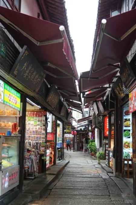 Old stone pedestrian North Street in Zhujiajiao Water Town, Shanghai. Traditional Chinese storefronts with red awnings line both sides, selling local snacks and souvenirs
