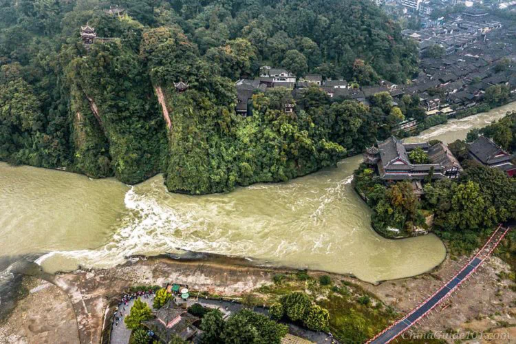 Aerial view of Baopingkou Water Outlet at Dujiangyan Irrigation System. The narrow man-made gorge cuts through the hillside, channeling Min River water, with historic buildings and Anlan Suspension Bridge in view