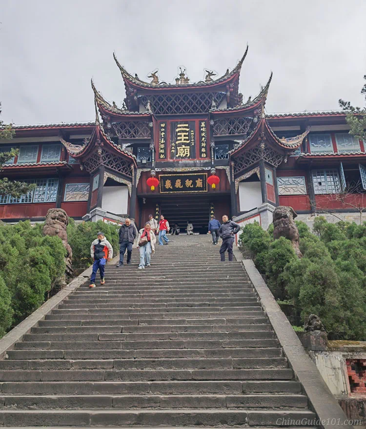 Front entrance of Erwang Temple at Dujiangyan. Grand traditional Sichuan Chinese temple building with upturned eaves, long stone staircase, stone lions and visiting tourists