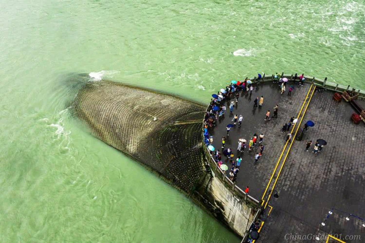 Aerial overhead shot of Yuzui Water-Dividing Dike at Dujiangyan Irrigation System. Tourists gather on the viewing platform beside the wedge-shaped stone dike splitting the Minjiang River