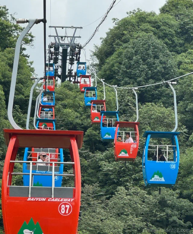 Colorful cabins of Baiyun Cableway winding over dense green forest on Qingcheng Back Mountain