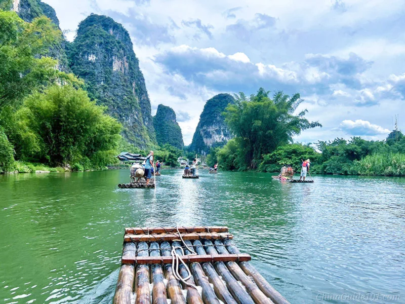 First-person view riding a bamboo raft on Yulong River, karst limestone peaks and green bamboo along the riverbank, Yangshuo