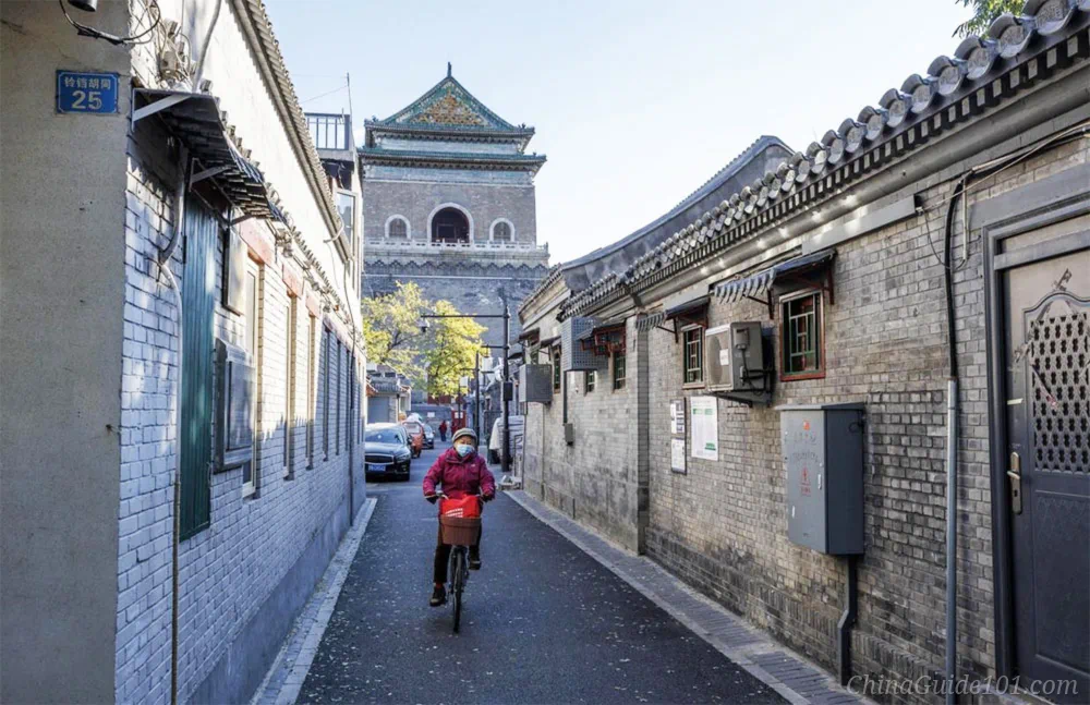 View of Beijing Bell Tower seen down Lingdang Hutong, a local resident cycling through the quiet grey-brick alley